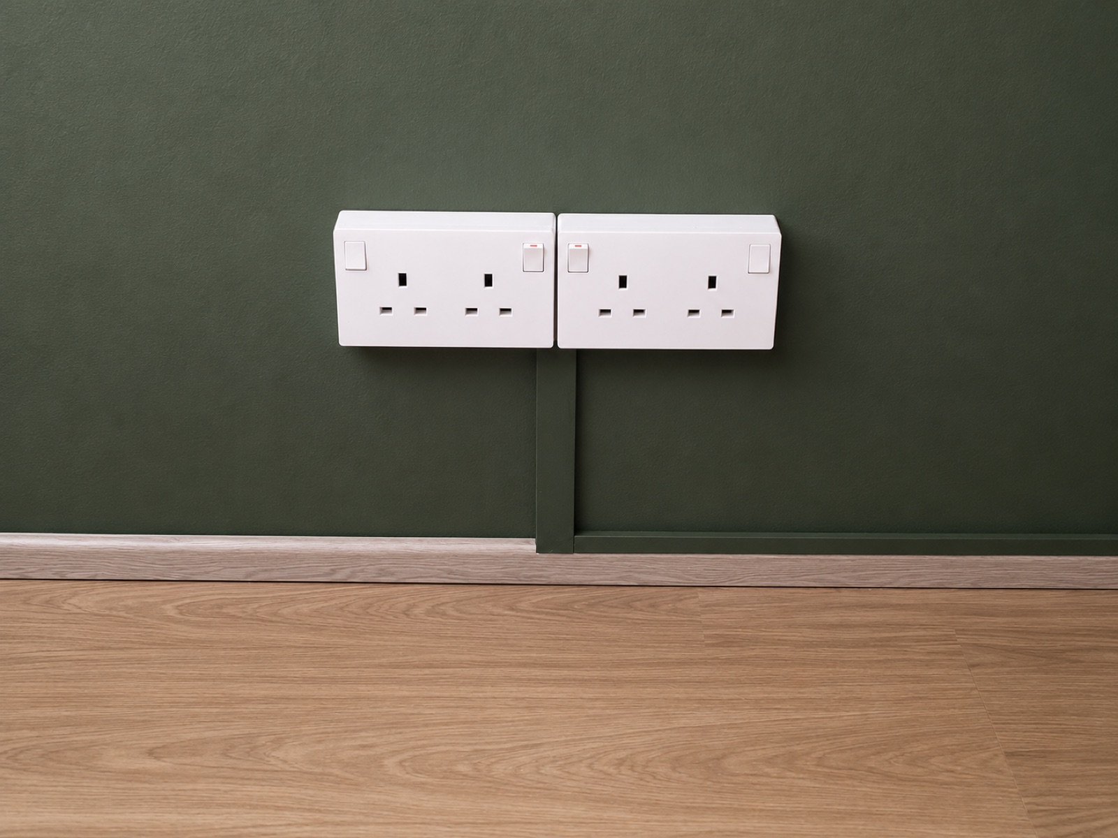 Twin double power sockets neatly finished on the green feature wall above wood-laminate flooring