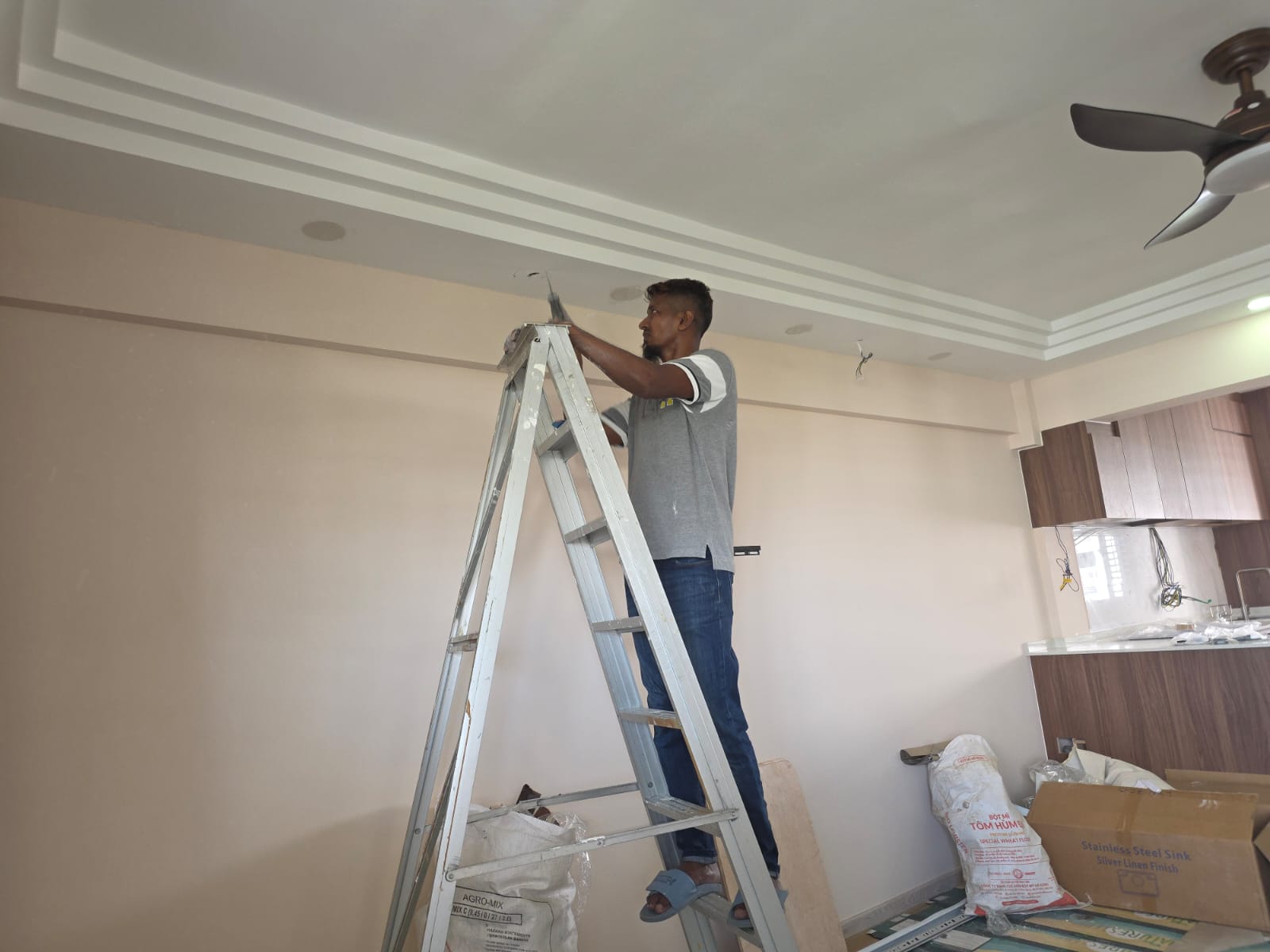 Unique Interior Design team member on a ladder finishing the false-ceiling cornice in an HDB living room