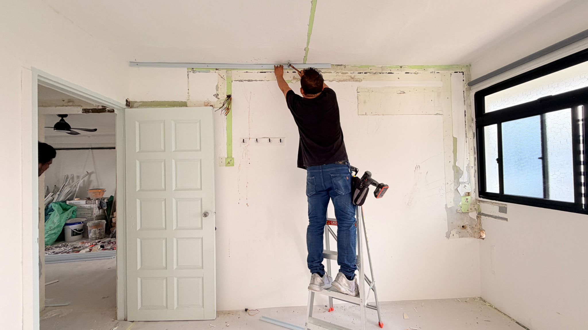 Renovation team member on a ladder installing concealed conduit at the wall-to-ceiling junction during first fix