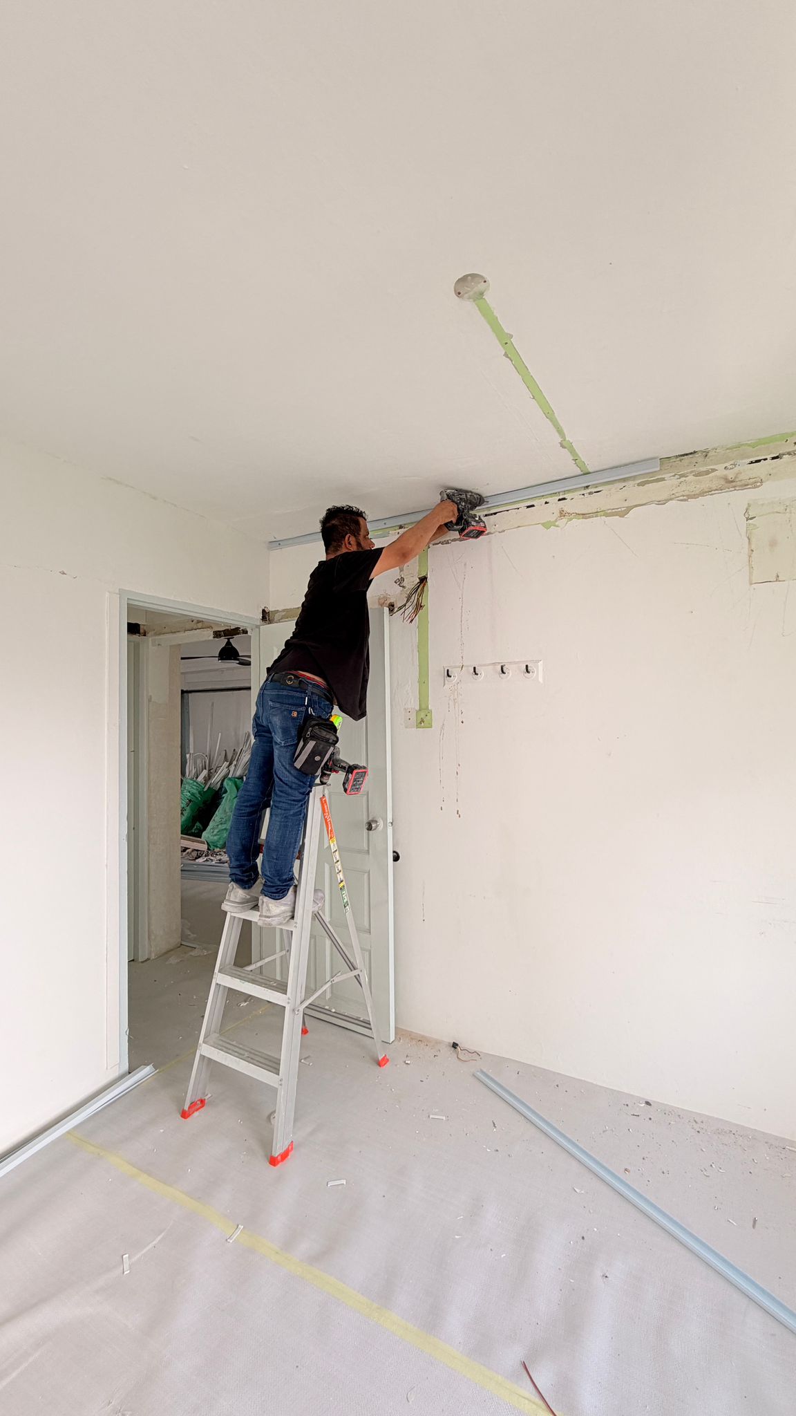 Renovation team member running concealed wiring along a chased route near the ceiling, with the floor fully protected
